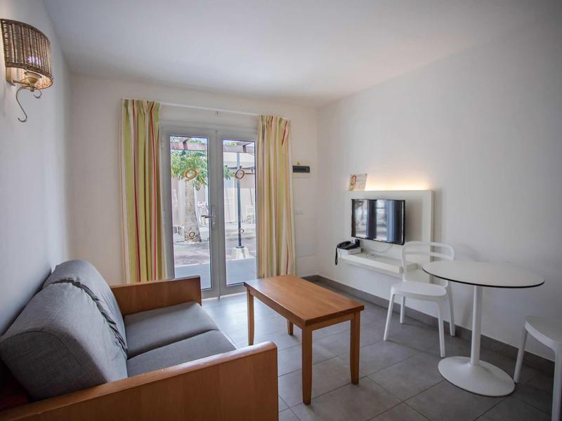 Bright, simple living room with sofa, wooden table, small white table, and window to the terrace.