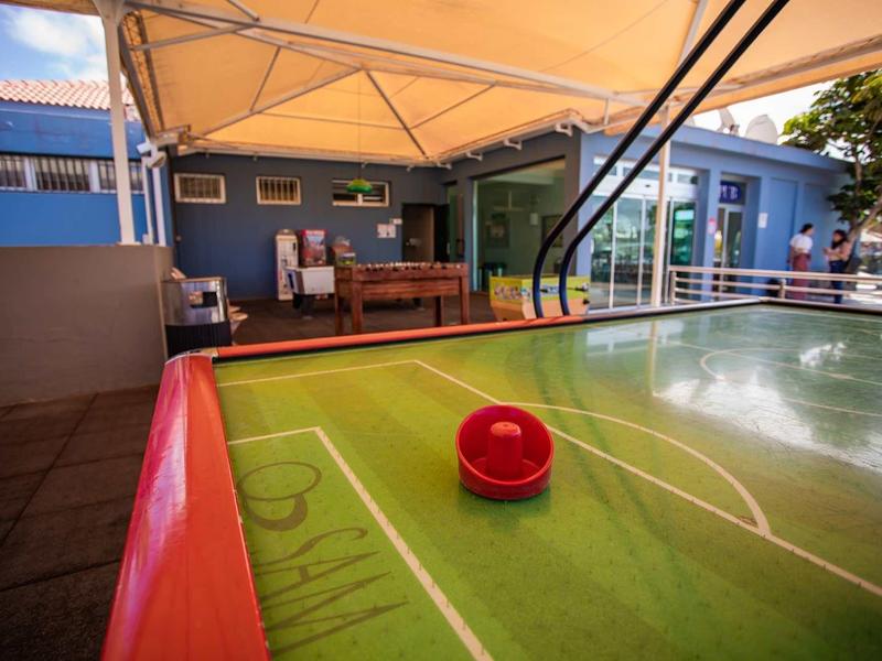 Air hockey table with red puck under a canopy on a terrace with seating area.