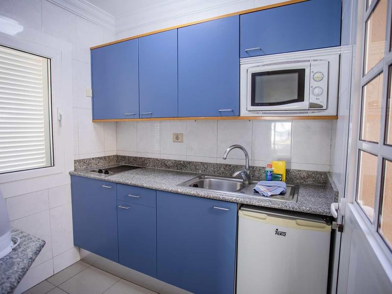 Compact kitchen with blue cabinets, microwave, sink, and mini fridge in a holiday apartment.