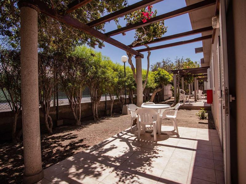 Sunny terrace with table and chairs under pergola beside a hotel building.