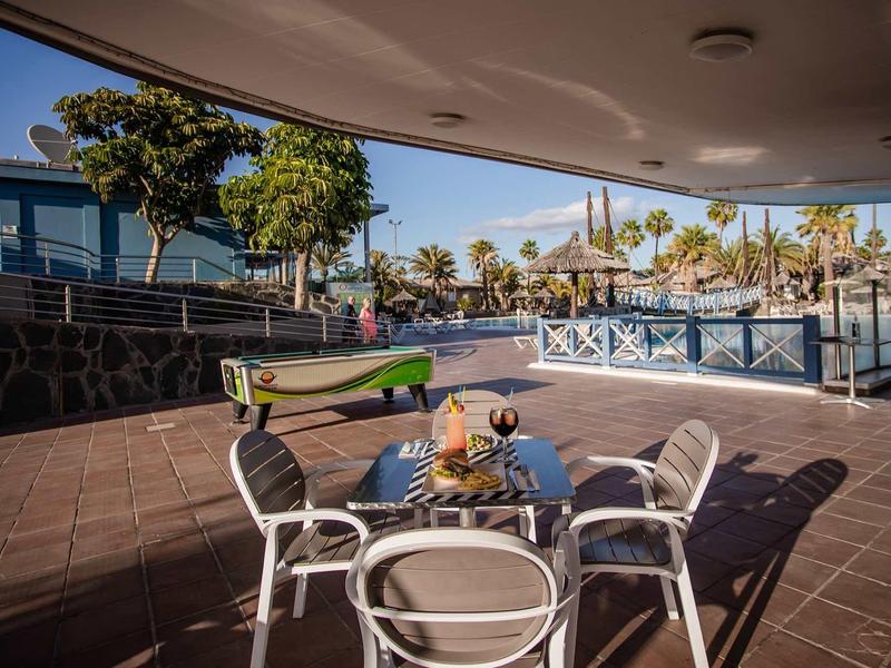 Terrace with table, chairs, and pool overlooking palm trees and blue sky.