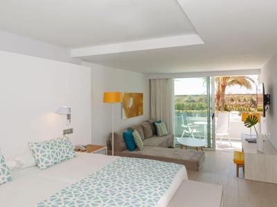 Chambre d'hôtel moderne avec lit double, canapé, télévision, balcon et vue sur des palmiers et la piscine