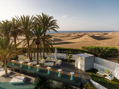 Luxuriöse Terrasse mit moderner Sitzgruppe, Palmen und Blick auf Dünenlandschaft im Sonnenschein.