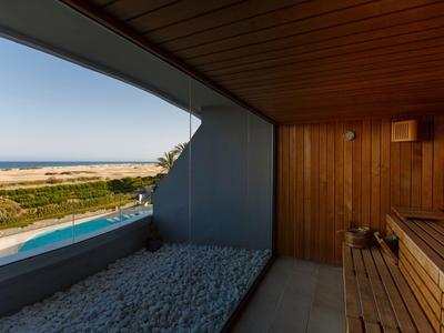 Sauna en bois avec vue sur piscine, plage et mer à l'horizon.