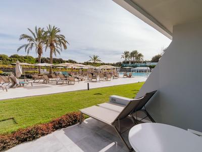 Balcon avec chaise et table surplombant la piscine, des chaises longues et des palmiers dans une zone d'hôtel.