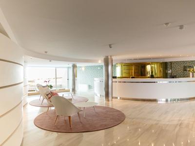 Lobby d'hôtel moderne avec chaises blanches et grand tapis rond rose.