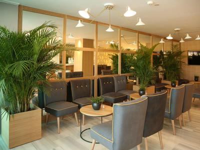 Salon d'hôtel lumineux avec fauteuils confortables et plantes vertes décoratives.