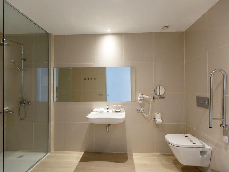 Salle de bain d'hôtel moderne avec douche vitrée, lavabo mural et toilettes suspendues.