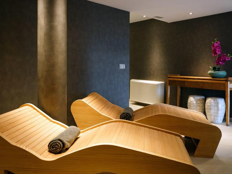 Chambre de spa avec deux chaises longues en bois et serviettes grises, ambiance chaleureuse.