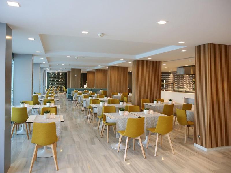 Salle à manger d'hôtel moderne avec chaises jaune moutarde et tables blanches.