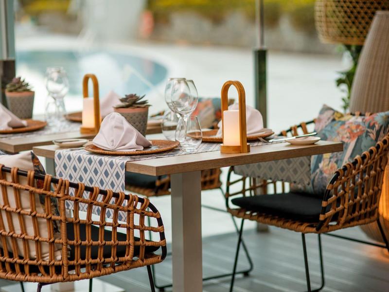Table élégante avec chaises en osier, décorée pour un repas à côté d'une piscine.