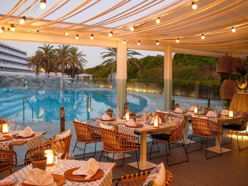 Terrasse de restaurant avec tables dressées près d'une piscine éclairée sous une pergola.