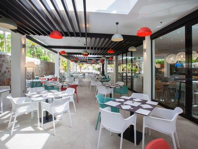 Nowoczesna restauracja hotelowa z białymi krzesłami, nakrytymi stołami i czerwonym oświetleniem.