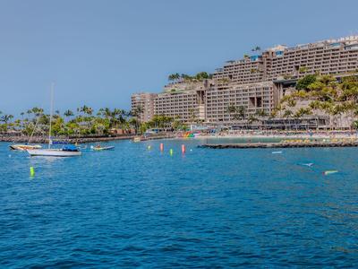 Große Hotelanlage an der Küste mit blauem Meer, Segelboot und klarem Himmel.
