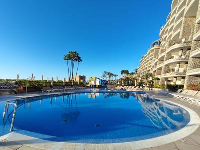 Großer, runder Pool vor modernen Hotelgebäuden unter klarem blauem Himmel