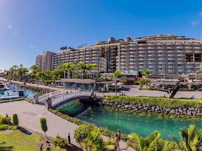 Modernes Hotelgebäude mit Brücke über einen Kanal und angrenzendem Yachthafen unter blauem Himmel