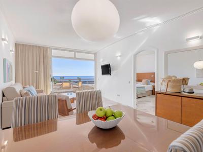 Heller Wohnbereich mit Sitzgelegenheiten und Meerblick, verbunden mit Schlafzimmer und Essbereich.