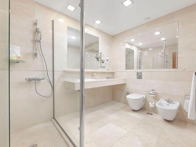 Modernes Badezimmer mit begehbarer Dusche, zwei Wandtoiletten und hellen Fliesen.