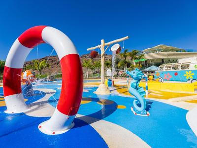 Bunter Wasserpark mit Spielgeräten und Rutschen unter blauem Himmel im Urlaubresort.