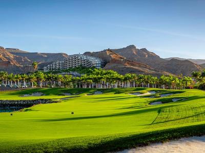 Grüner Golfplatz mit Bergen im Hintergrund unter klarem blauem Himmel