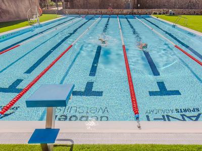 Ein Schwimmbecken mit Bahnen, umgeben von grünem Gras und Schwimmbrettern am Beckenrand.