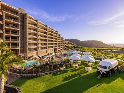 Modernes Hotelgebäude neben Pool und grünem Rasen mit entspannenden Sitzbereichen und Meerblick.