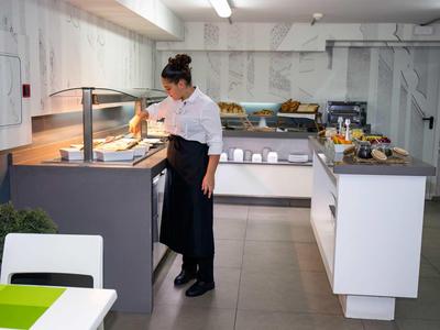 Eine Frau in Kochkleidung steht an einem Buffet in einem modernen, hellen Speisesaal.