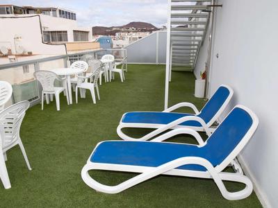 Dachterrasse mit grünem Kunstrasen, weißen Plastikstühlen, Tischen und blauen Liegestühlen.
