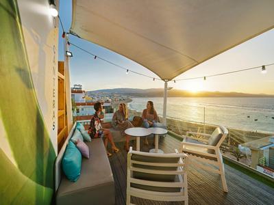 Terrasse mit Sitzmöbeln, weißem Sonnensegel und Blick auf Sonnenuntergang am Meer.