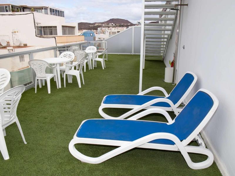 Dachterrasse mit grünem Kunstrasen, weißen Plastikstühlen, Tischen und blauen Liegestühlen.