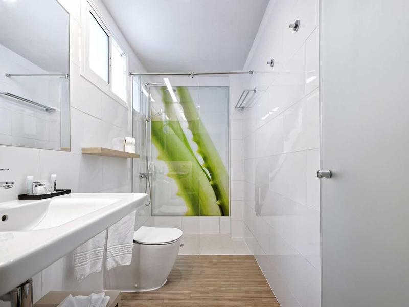 Modernes weißes Badezimmer mit Holzoptik-Boden, großer Spiegel, Waschtisch, Toilette und Duschvorhang.