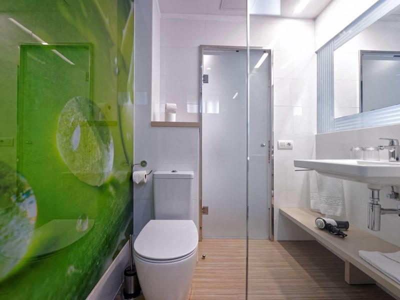 Modernes Badezimmer mit Glasdusche, weißem Waschbecken, Toilette und grünem Akzent an der Wand.