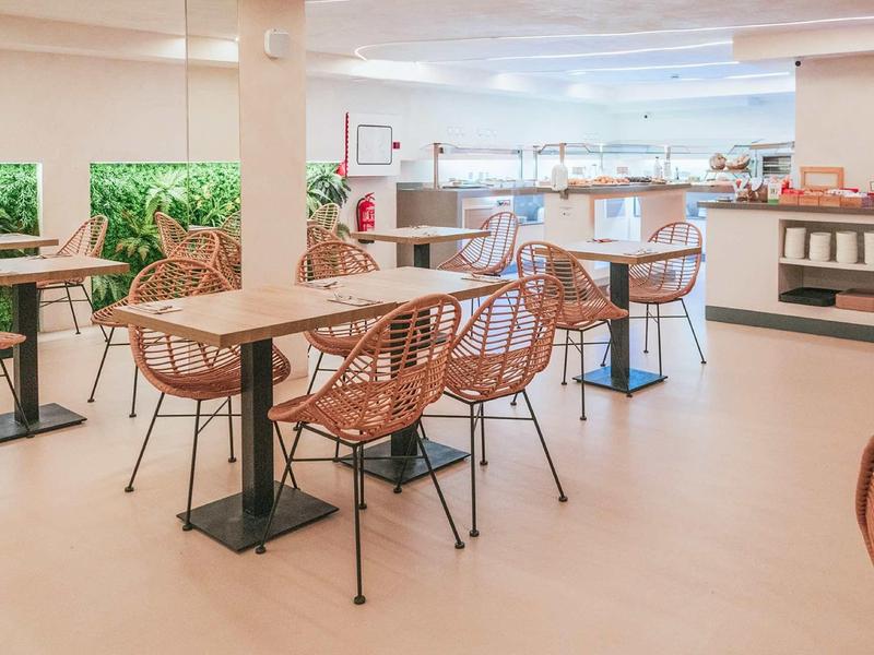 Moderner heller Cafébereich mit Korbstühlen und Tischen auf hellem Boden und Kaminwand.