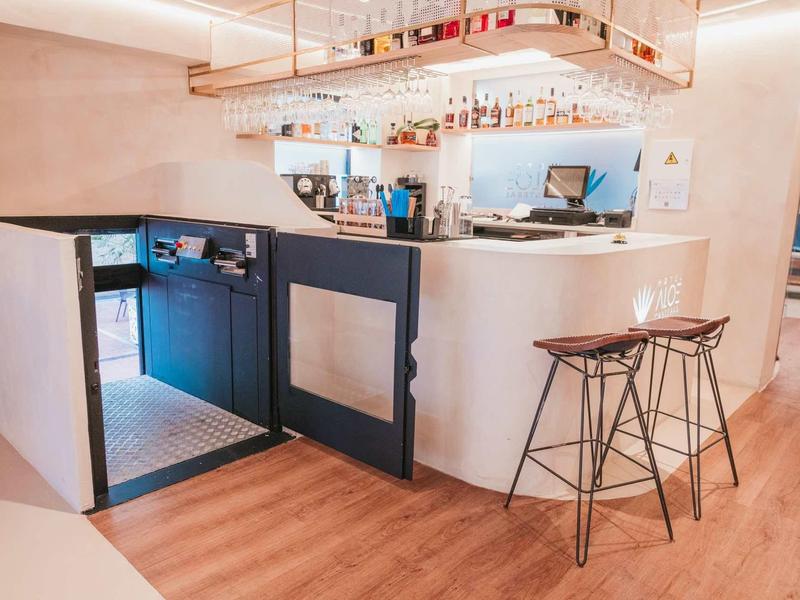 Moderner Empfangstresen mit weißen Fronten und zwei hohen Barhockern auf Holzboden.