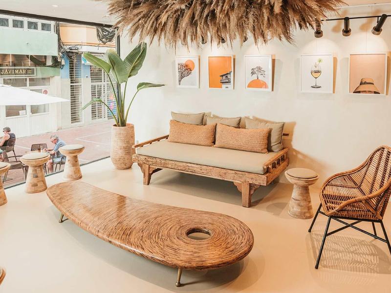 Heller Wohnbereich mit Rattanmöbeln, ovalem Holztisch, großer Pflanze und Bildern an der Wand.