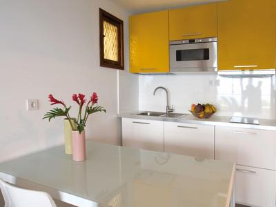 Kleine moderne Küche mit gelben Hängeschränken, weißer Arbeitsplatte und rosa Blumen auf Tisch.