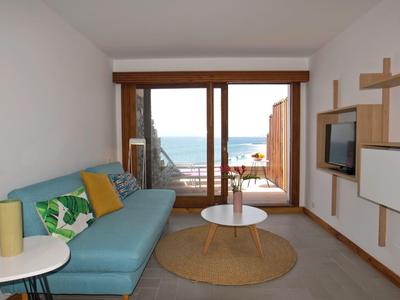 Helles Wohnzimmer mit blauer Couch, Rundtisch, Teppich und großem Fenster mit Meerblick.