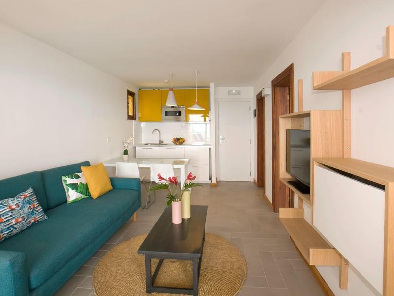 Modern eingerichtetes Wohnzimmer mit grünem Sofa, Couchtisch und offener Küchenzeile.