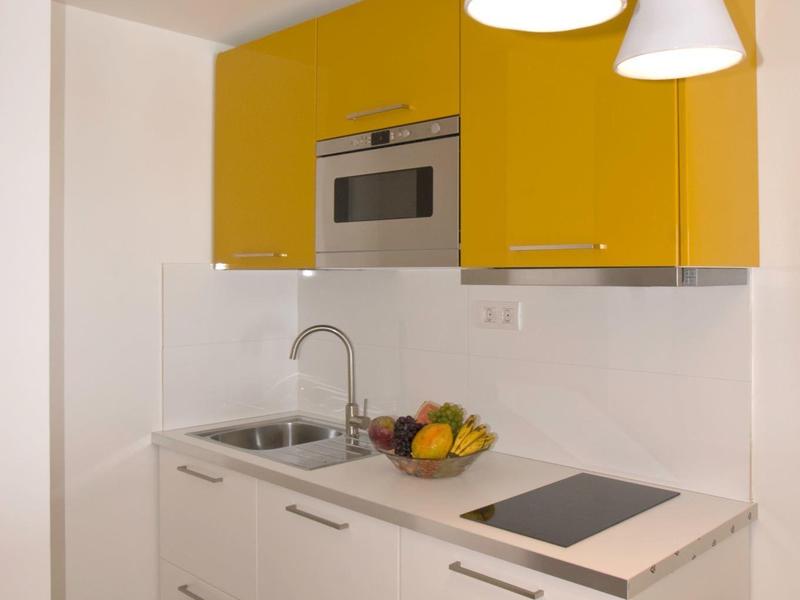 Moderne kleine Küche mit gelben Oberschränken, weißer Arbeitsplatte und drei Hängeleuchten.