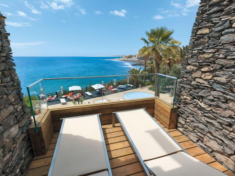 Terrasse mit Liegestühlen bietet Meerblick und Blick auf Strand und Palmen.