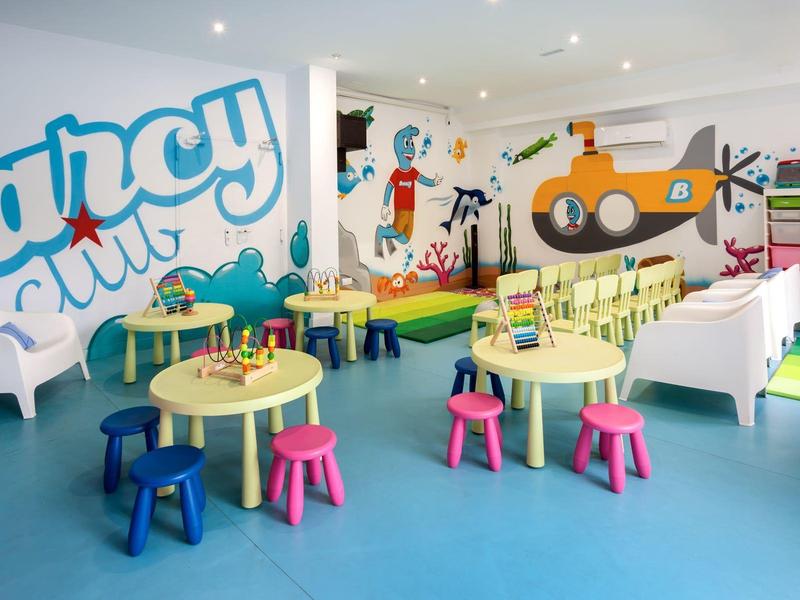 Colorful children's playroom with tables, chairs, and wall illustrations in bright setting