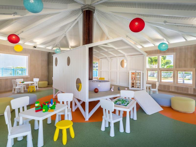 Bright, colorful playroom for children with tables, chairs, slide, and colorful balloons.