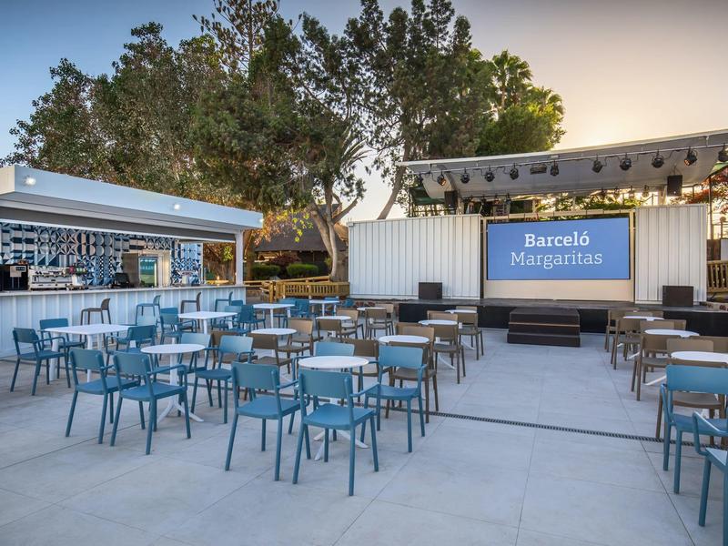 Outdoor cocktail bar with blue chairs and wooden tables in front of trees at sunset.