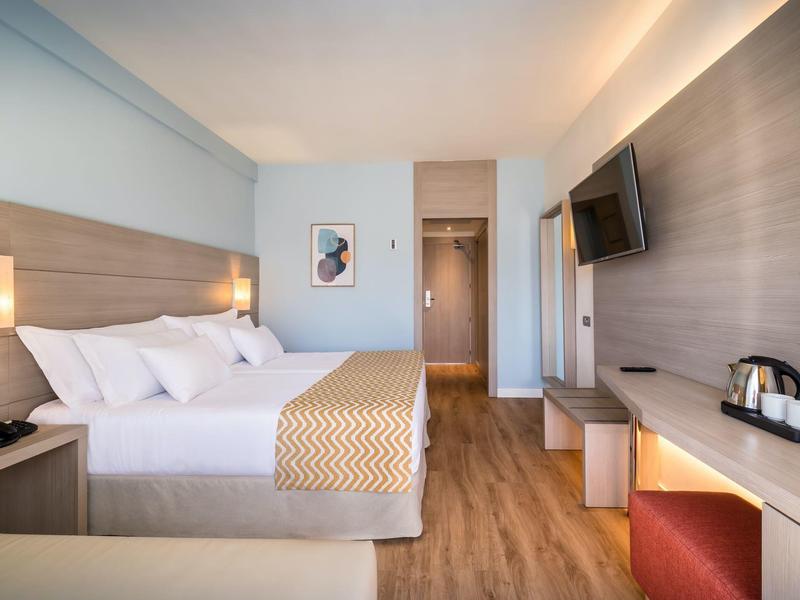 Modern hotel room with large bed, wooden floor, and wall-mounted TV.