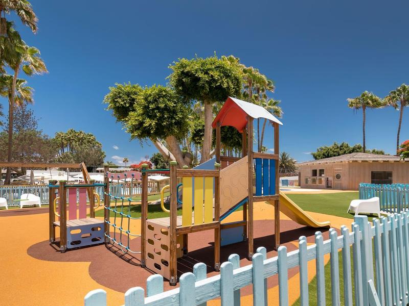 Colorful children's playground with climbing frame and slide, surrounded by a white picket fence.