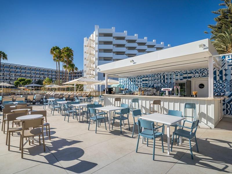 Modern hotel terrace with chairs, tables, and bar under a blue sky.