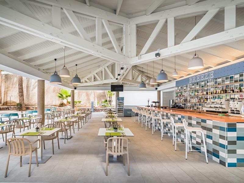 Modern, bright restaurant with white wooden beams and a long bar with colorful tiles.