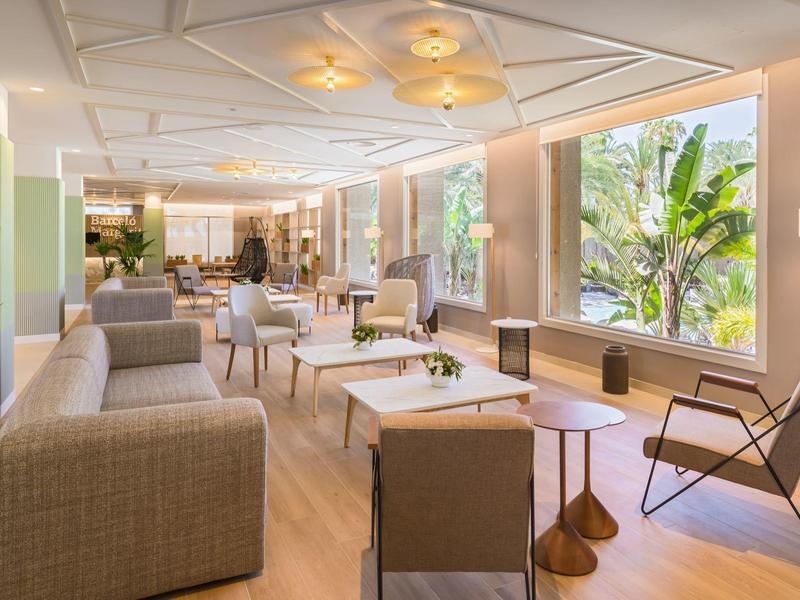 Bright, modern hotel lounge area with seating and views of green plants.