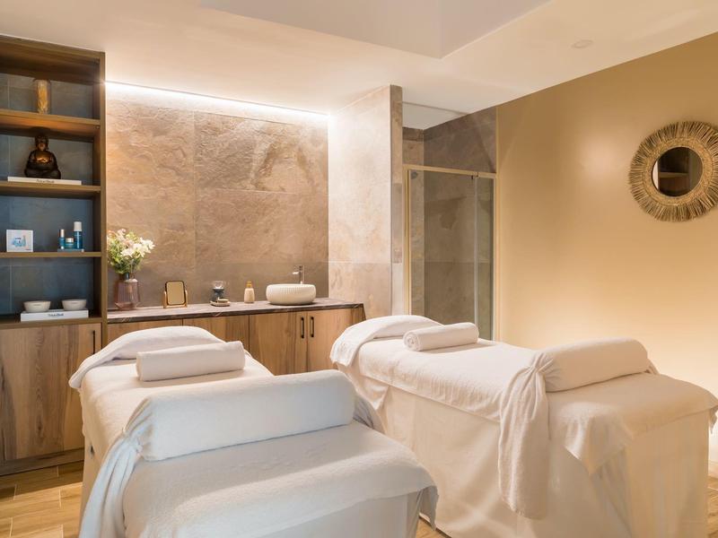 Cozy spa room with two treatment beds, soft lighting, and warm wooden accents.