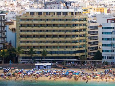 Edificio di hotel moderno vicino a una spiaggia affollata con ombrelloni e bagnanti